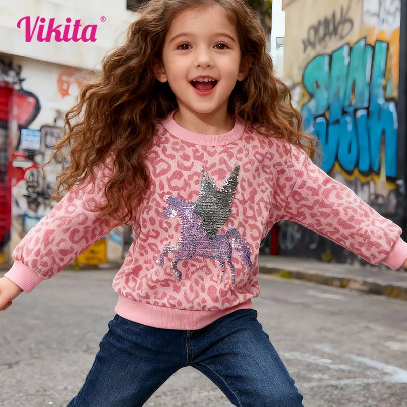 Mädchen trägt einen rosafarbenen Einhorn Pullover mit Leopard-Print und reversiblen Einhorn-Pailletten auf der Brust