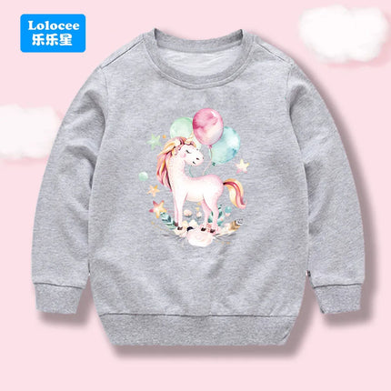 Kind in einem grauen Einhorn Hoodie mit einem bunten Cartoon-Ballon-Einhorn-Print auf der Vorderseite, das Freude und Komfort ausstrahlt.