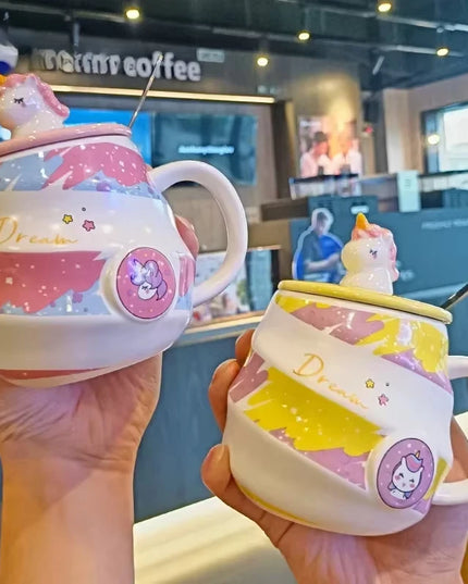 Weiße Keramik Einhorn Tasse mit Deckel und Löffel, verziert mit einem Cartoon-Einhornkopf und Regenbogen.
