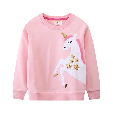 Mädchen in einem blauen Riesen Einhorn Sweatshirt mit farbenfroher Einhorn Stickerei, das fröhlich lächelt und spielt.
