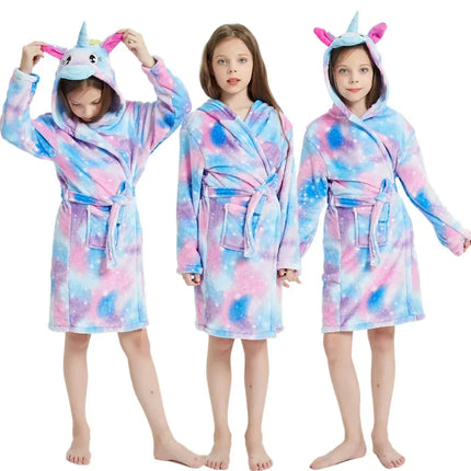 Mädchen in einem flauschigen Einhorn Pyjama in hellen Farben, gemütlich auf einem Sofa sitzend