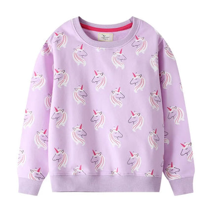 Mädchen in einem lila Riesen Einhorn Sweatshirt mit einem verspielten Einhorn-Motiv, das fröhlich die Arme ausbreitet.